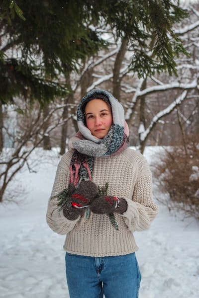 白天，穿着白色针织毛衣、戴着红领巾的女人站在雪地上